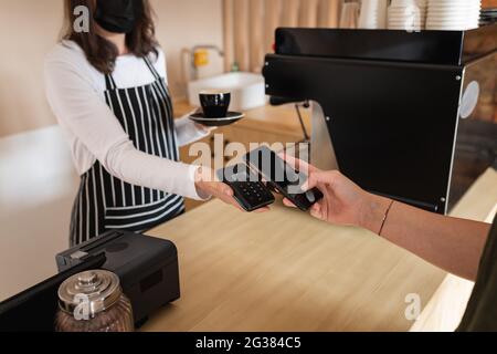 Midsection of caucasian customer paying by smartphone to caucasian female business owner Stock Photo