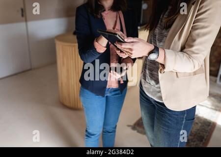 Midsection of two caucasian women in casual clothes standing, using tablet, talking Stock Photo