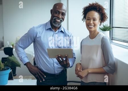 Portrait of two diverse male and female business colleagues smiling and using tablet Stock Photo