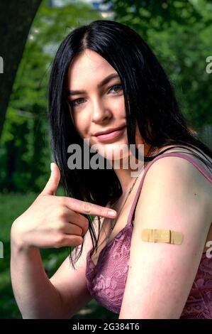 Smiling female with band-aid on arm after vaccination.. Woman feeling positive after getting vaccinae. Happy teenage girl outdoor Stock Photo
