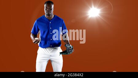 African american male baseball pitcher holding a ball against spot of light on orange background Stock Photo