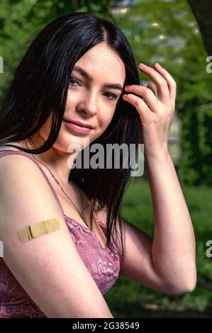 Smiling female with band-aid on arm after vaccination.. Woman feeling positive after getting vaccinae. Happy teenage girl outdoor Stock Photo