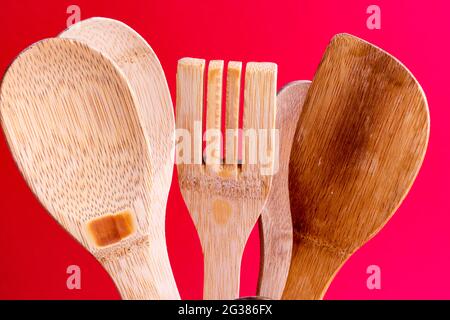 Used wooden kitchen utensils like spoon, spatula and fork on red background. Stock Photo