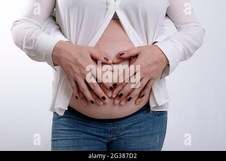 Pregnant woman and her husband holding hands on belly. Couple expecting a baby in studio with white background Stock Photo