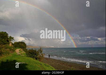 beautiful rainbow over the sea, cloudy sky, horizon, person walks on the beach Stock Photo