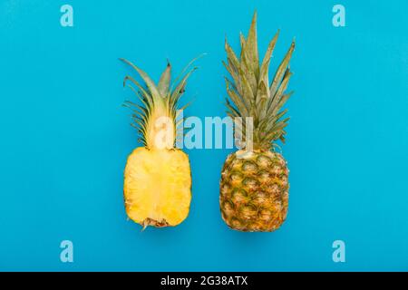 Pineapple fruit on blue summer background. A whole tropical pineapple and half fruit in minimalist style on summer bright blue background. Flat lay Stock Photo
