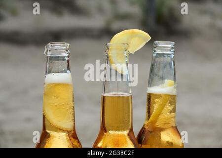 three bottles of blonde beer with lemon inside on the beach background Stock Photo