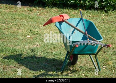 Gardening tools. Rake and garden shovel lying on wheelbarrow in the garden Stock Photo