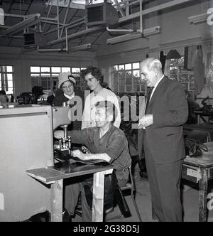 1960s, historical, inside an indistrial unit, two lady local councilors and a company Director, standing by a worker, a  former mineworker being re-employed in industry, using a large machine to stitch or seal leather goods such as bags together, Cowdenbeath, Fife, Scotland. Stock Photo