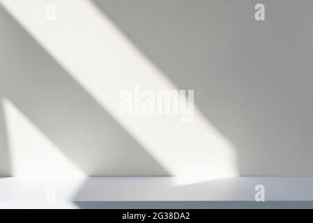 Sunlight and abstract shadows on the wall and white desk. Silhouette of lines on blank surface, mockup, space for text. Stock Photo
