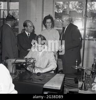 1960s, historical, inside an indistrial unit, local councilors and a company Directors, standing by a female worker,  being re-employed in industry, using an industrial type sewing machine to stitch leather sheets, Cowdenbeath, Fife, Scotland. Stock Photo