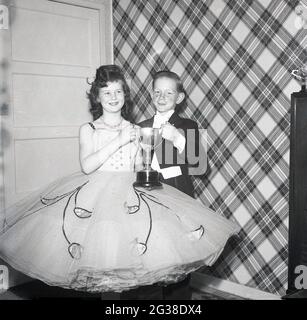 1965, historical, inside a room, big smiles as two young child dancers, a young girl in a frilly dress and a freckled young boy in a dress suit, stand proudly holding their trophy, Oakley Smyth of Sligg Street, Cowdenbeath, Scotland, UK. Note the tartan wallpaper! Stock Photo