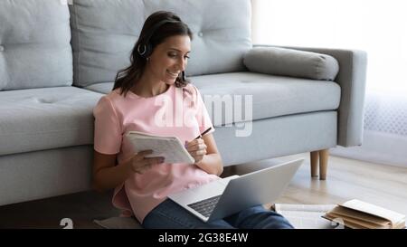 Smiling Arabian woman in headphones taking notes, using laptop Stock Photo