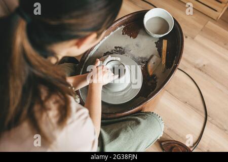 Top view of female pottery maker works in clay studio on pottery wheel. Handmade, design and workshop concept. Stock Photo