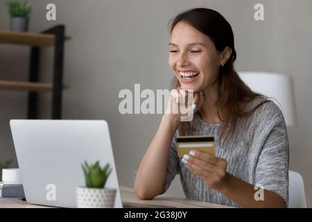 Overjoyed woman holding credit card, using laptop, excited by success Stock Photo