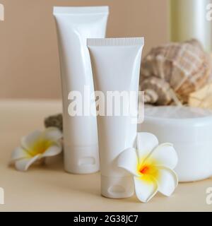 Natural beauty cosmetic tube mockup product for skincare with sea shell tropical plumeria flowers on stone pedestal beige background. Natural body Stock Photo