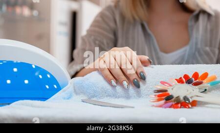 Woman with artificial acrylic nails picks up new polish color during manicure procedure. Manicure process in beauty salon. Hygiene beauty of hands in Stock Photo