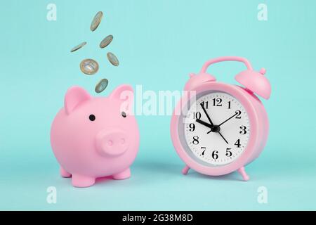 Time, Savings, Time is Money. Pink Piggy Bank Piggy Bank with Falling Coins and alarm clock, concept of savings. Financial savings and banking economy Stock Photo