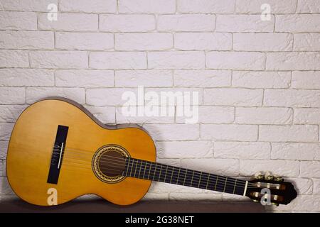 Below, against a decorative wall made of light bricks, lies a wooden acoustic guitar. There is a place for advertising above it. Stock Photo