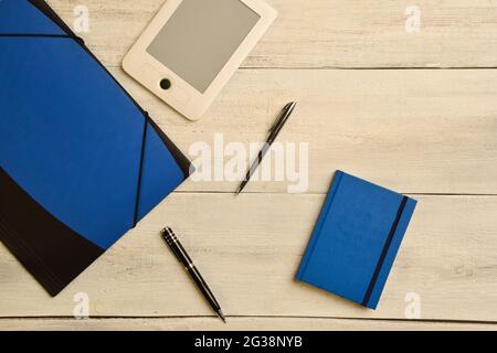 A folder for documents, an electronic book, two pens and a note book lie on a wooden beige table Stock Photo