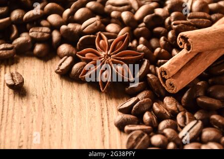 Anise, cinnamon and many coffee beans lie on a brown wooden table. There is an empty space at the bottom left. Stock Photo