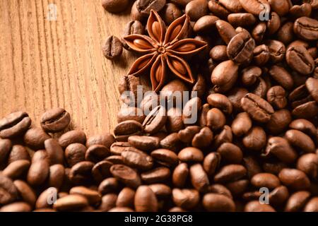 Anise and a lot of coffee beans lie on a wooden brown table. There is an empty space at the top right. Stock Photo