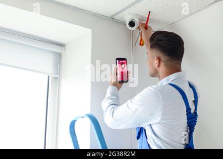 Worker with mobile phone checking alarm system indoors Stock Photo