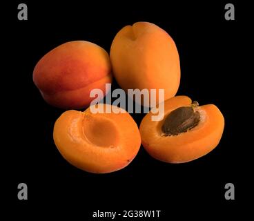 A bunch of ripe Apricot fruits, two whole and one halved, on a black background, isolated Stock Photo