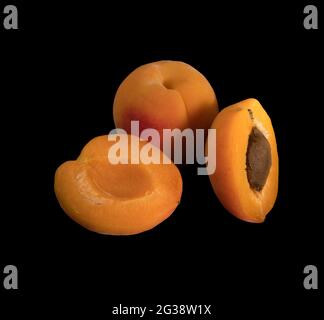 Ripe Apricot fruits, one whole apricot and two divided apricot pieces, on a black background in isolation Stock Photo