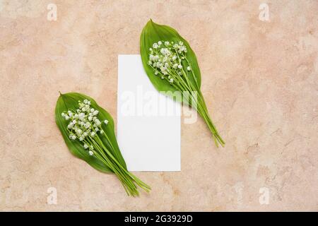 Beautiful lily-of-the-valley flowers and blank card on color background Stock Photo