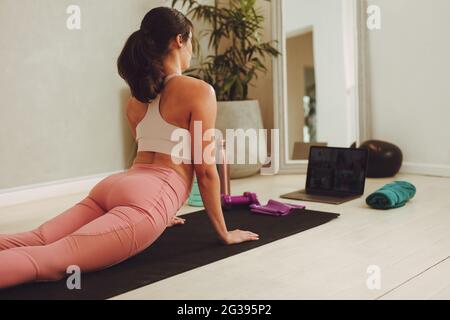 Woman exercising watching online exercise session on her laptop. Female in fitness wear doing yoga watching online class at home. Stock Photo