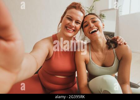 Smiling women taking self portrait at health club. Female friends in fitness studio taking selfie. Stock Photo