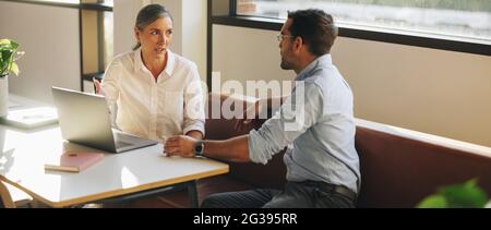 businesswoman sharing project details on laptop to colleague at office desk. Mature woman using laptop to explain new proposal to business partner in Stock Photo