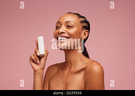 Good looking woman holding beauty product. African american woman presenting cosmetic cream on pink background. Stock Photo