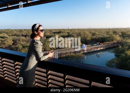 Asian female tourist visiting Mangrove walk seaside promenade public park in Jubail island Abu Dhabi the capital city of United Arab Emirates Stock Photo