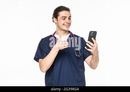Medicine, healthcare and technology concept. Happy smiling doctor or male nurse in blue uniform with stethoscope having video call on phone over white Stock Photo