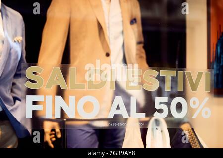 Sale 50 off sticker on glass window display with mannequin in italian fashion store. Discount sign showcase of public cloth store Stock Photo