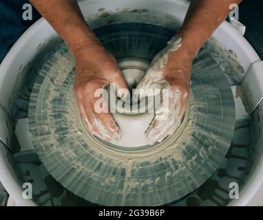 hands shaping pottery on a wheel with messy hands in a studio Stock Photo