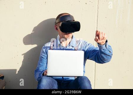 Businessman examining virtual reality simulator while using laptop Stock Photo