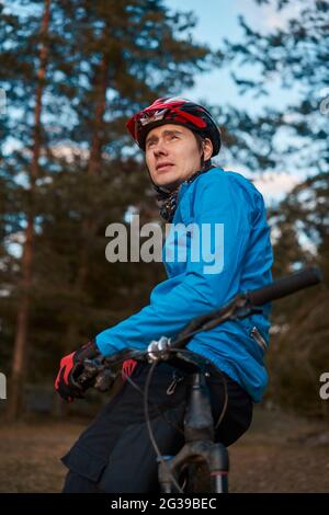 Man wearing bicycle helmet standing in forest, spending free vacation time on a bicycle trip in a forest. Stock Photo