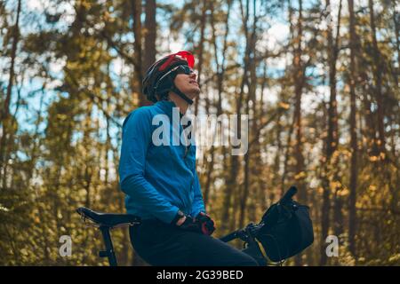 Man wearing bicycle helmet standing in forest, spending free vacation time on a bicycle trip in a forest. Stock Photo