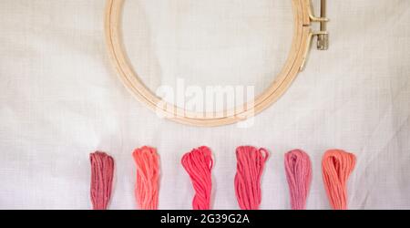 The linen Canvas for embroidery with a cross embroidered in a round wooden hoop, multi-tone pink-colored thread mouline thread, For hobby and freetime Stock Photo