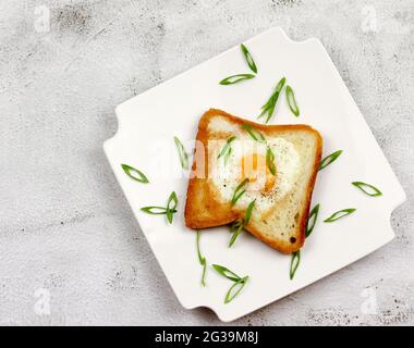 Egg in a hole toast with black pepper and green onions on a white rectangular plate on a light gray background. Top view, flat lay Stock Photo