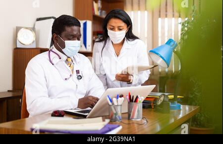 Two physicians in protective masks working on laptop in office Stock Photo
