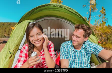 Camping campers Asian woman applying sunscreen sun cream sunblock suntan lotion in tent smiling happy outdoors in forest. Happy biracial girl living Stock Photo