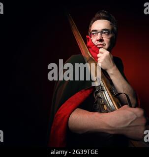 Soldier of past times standing sideways with his rifle slung over his shoulder, holding collar of cape and looking back Stock Photo