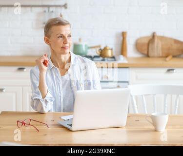 Thoughtful senior woman with laptop looking away Stock Photo