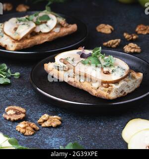 Bruschetta with gorgonzola blue cheese, pears and walnuts on a dark plates on dark background. Appetizing bruschetta. Mediterranean cuisine. Stock Photo