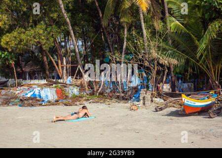 Female foreign tourist sunbathing on beach beneath palm trees, Palolem, Goa, India Stock Photo