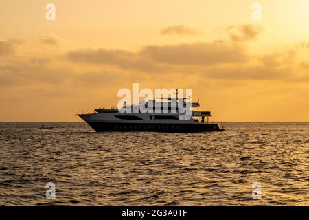 Dark silhouette of a diving boat with orange sunset over the Red Sea, cloudy sky and calm sea. Stock Photo